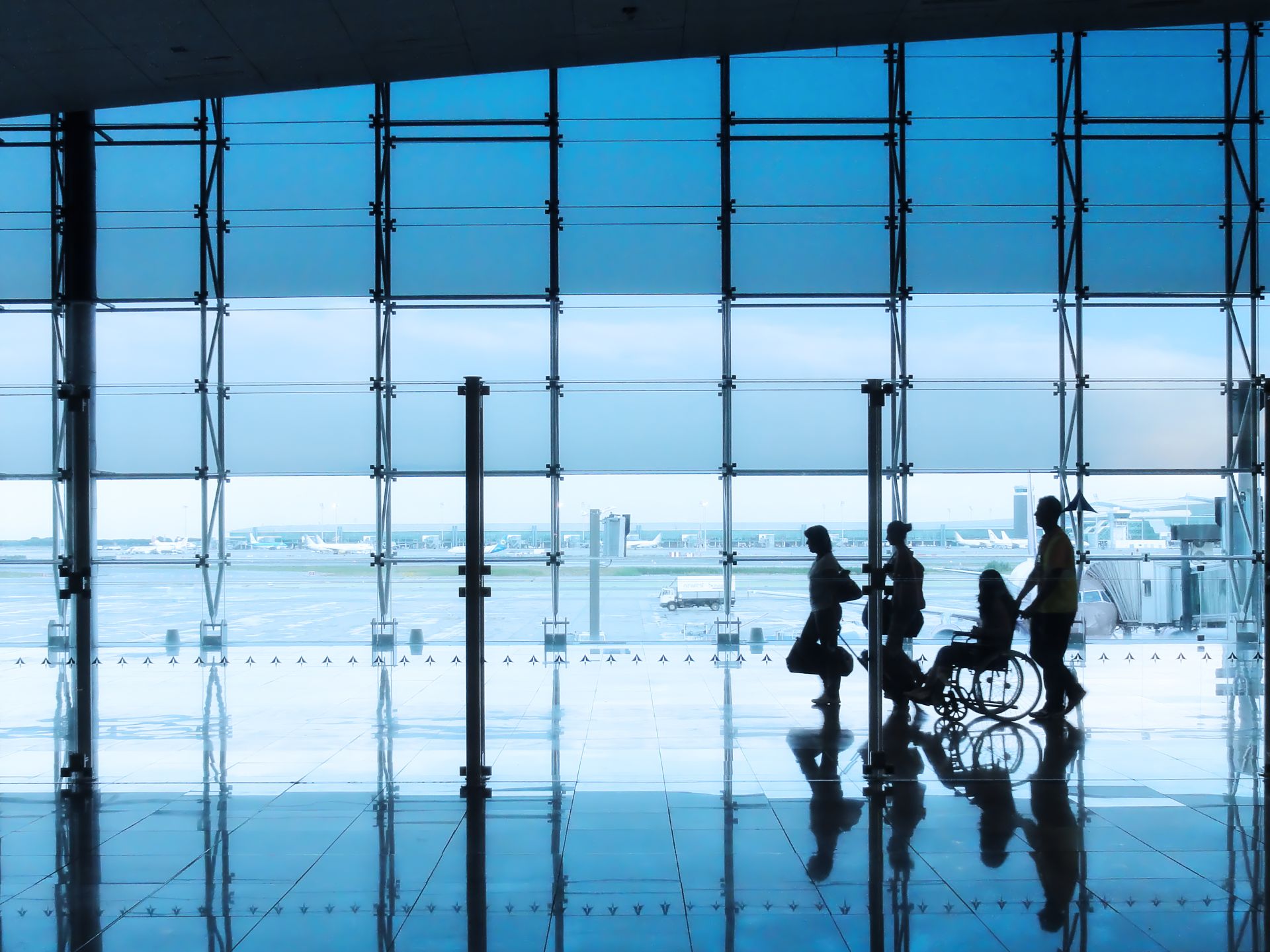 iStock-153535825 web res Silhouettes of travelers, including someone in a wheelchair, move through a bright airport terminal with large glass windows showing the runway.
